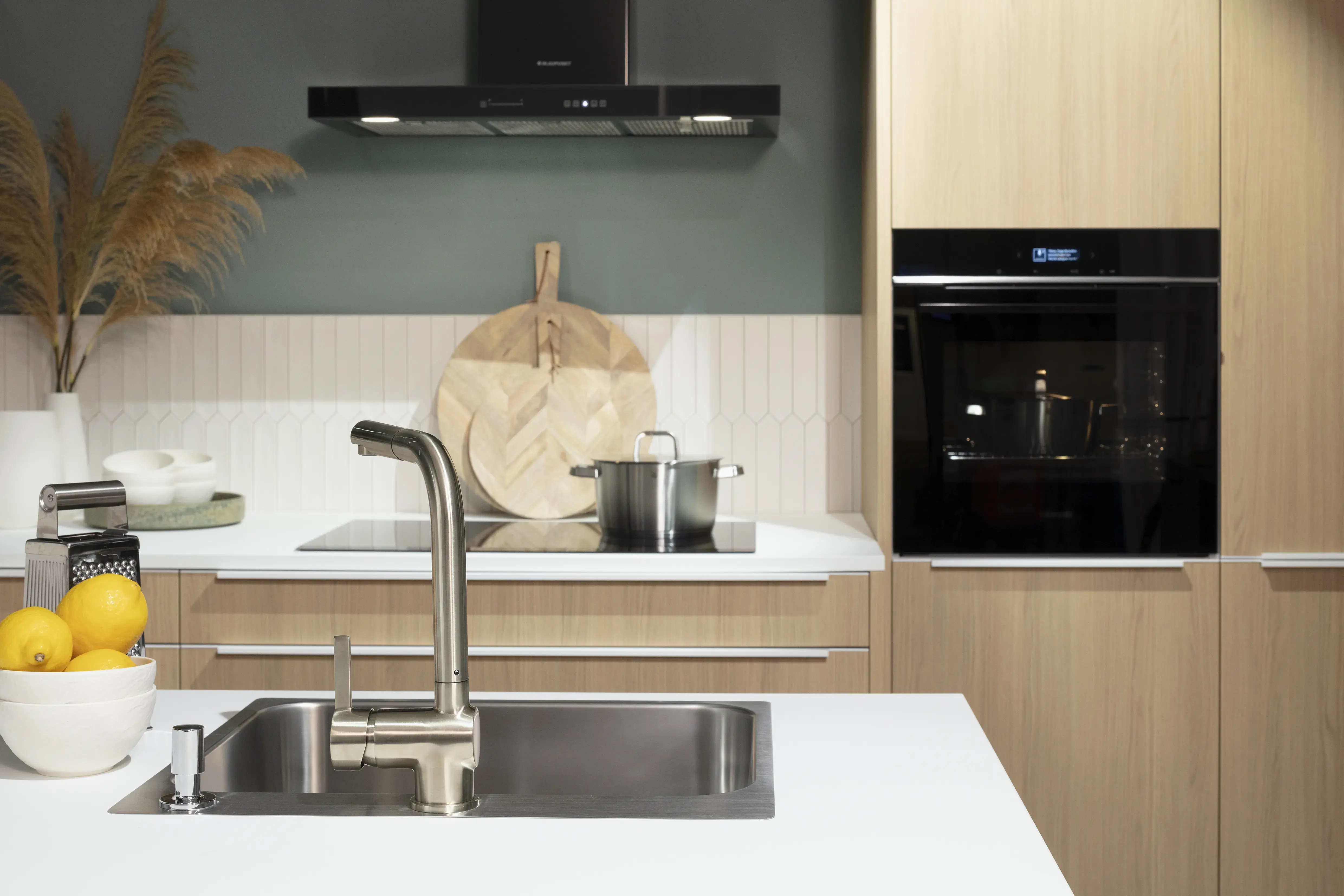 Moderne Küche mit Edelstahlspüle, Backofen und Zitronenschale auf weißer Arbeitsplatte.